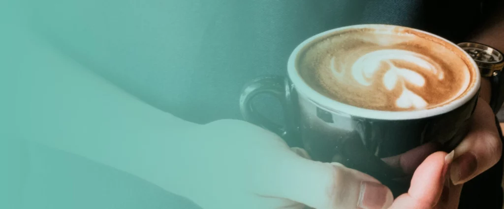Hands holding a coffee cup with latte art facing away from the viewer